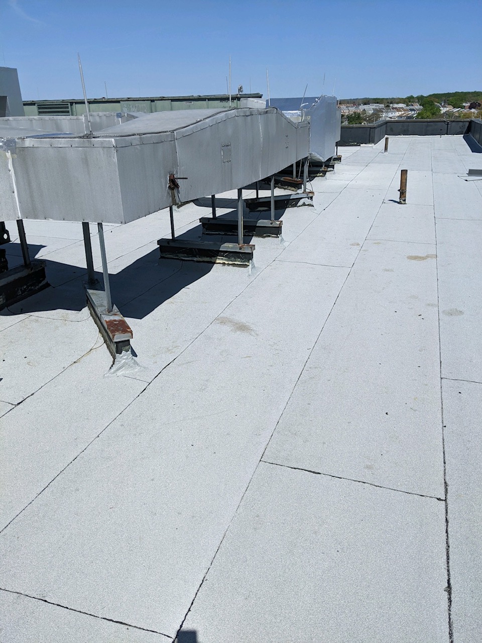Light gray flat roof laid in overlapping rolls, with lap lines running across it and rooftop equipment along one side