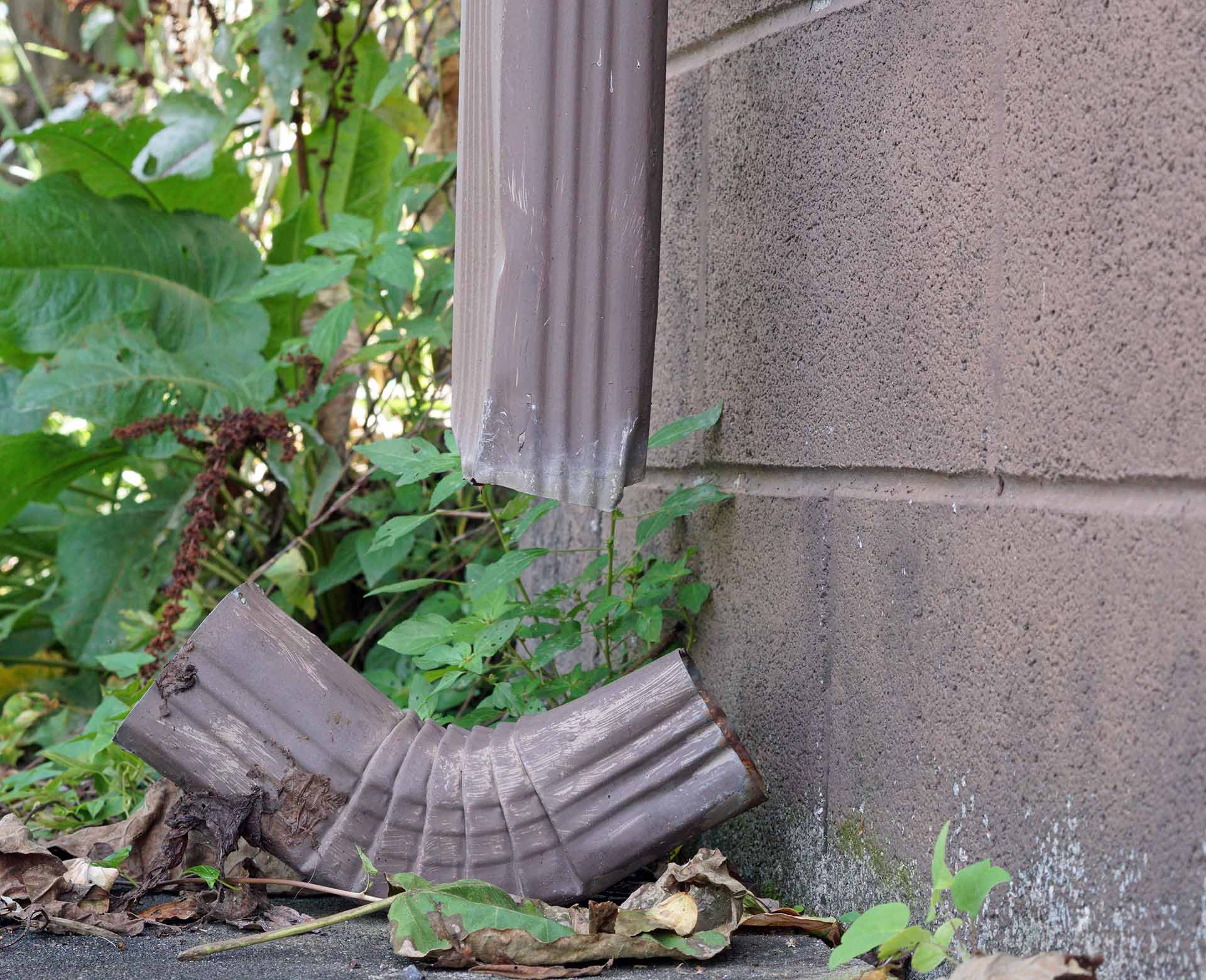 Broken downspout elbow lying on the ground beside a block wall