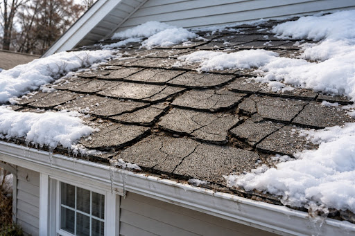 Cracked and curled asphalt shingles on a residential roof after a winter storm